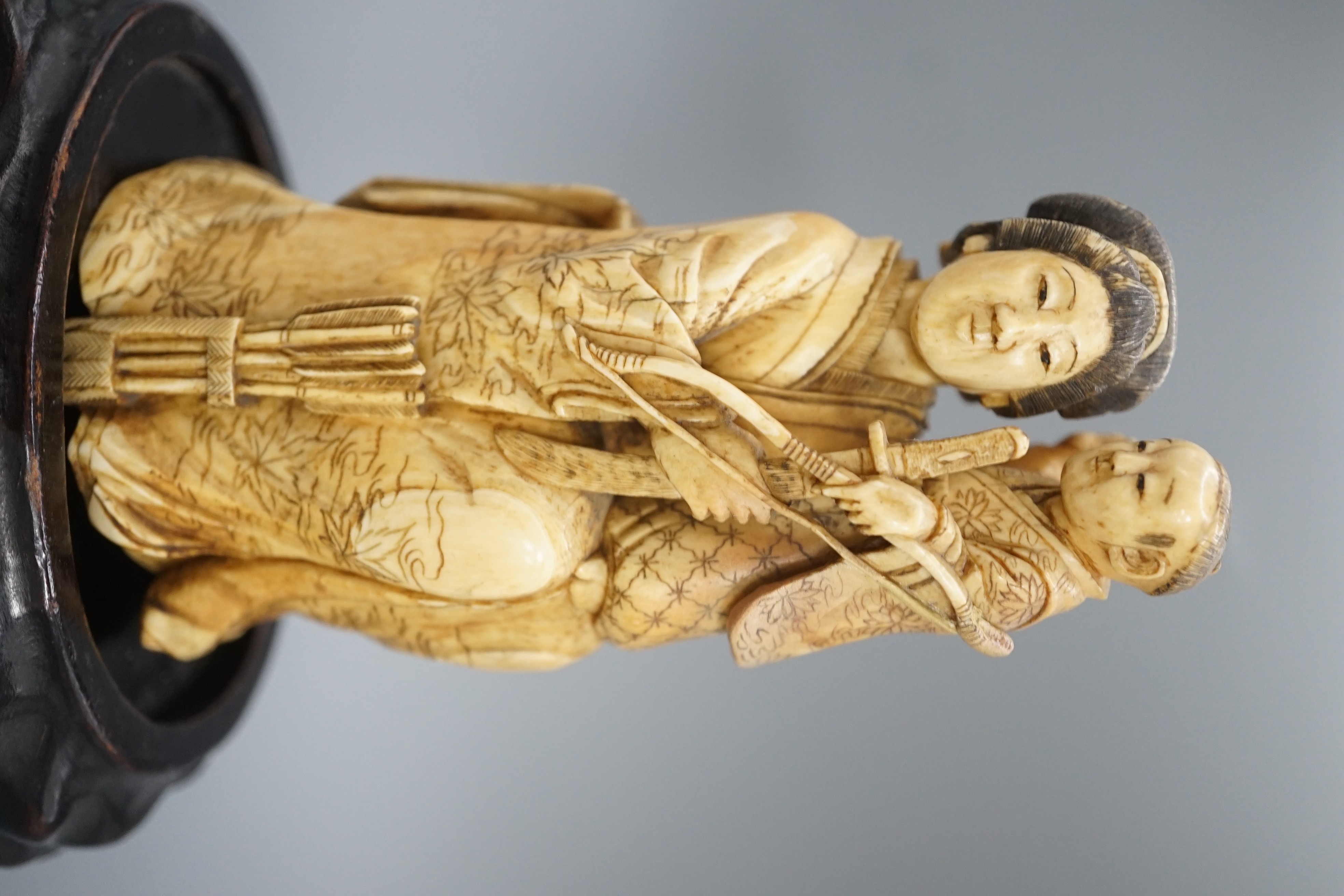 A Japanese ivory okimono of a lady holding a boy with a bow and arrow, Meiji period, restoration 12cm, wood stand
